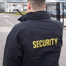 A security guard in a black jacket facing away from the camera